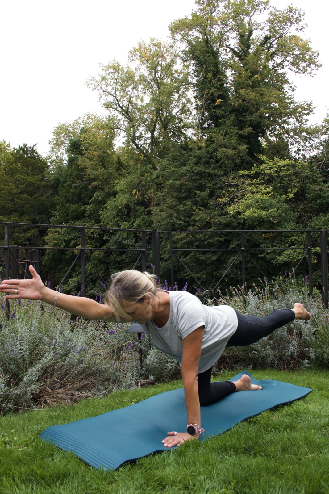 Nicky performing a Pilates bird-dog pose on a mat outdoors